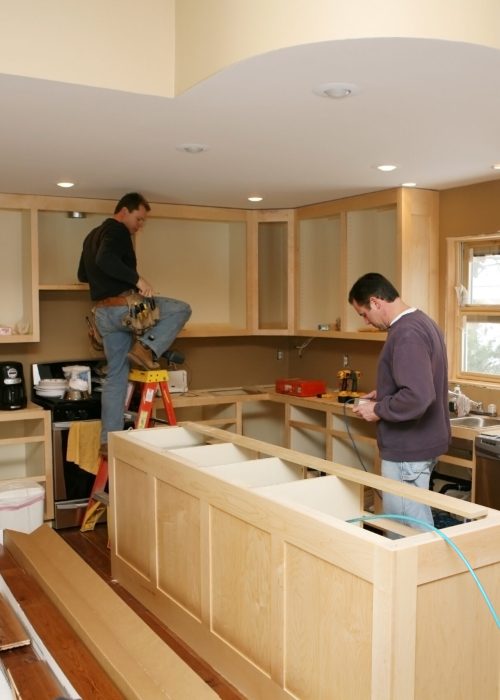 Cabinet maker installing custom made kitchen island and cabinets, while electrician installs in-cabinet lighting. 

Very shallow DOF quickly drops off to nice soft focus.